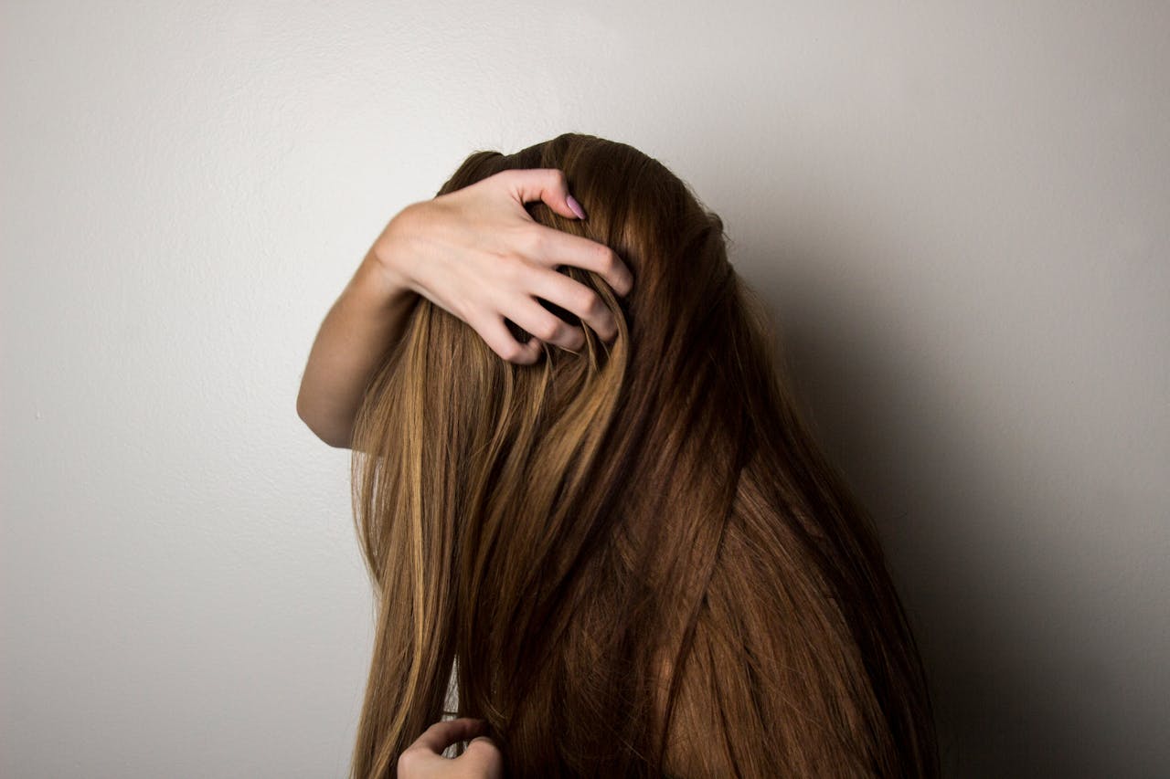 who-we-are An artistic close-up of a woman's long brunette hair held gently by her hand, emphasizing texture and color.